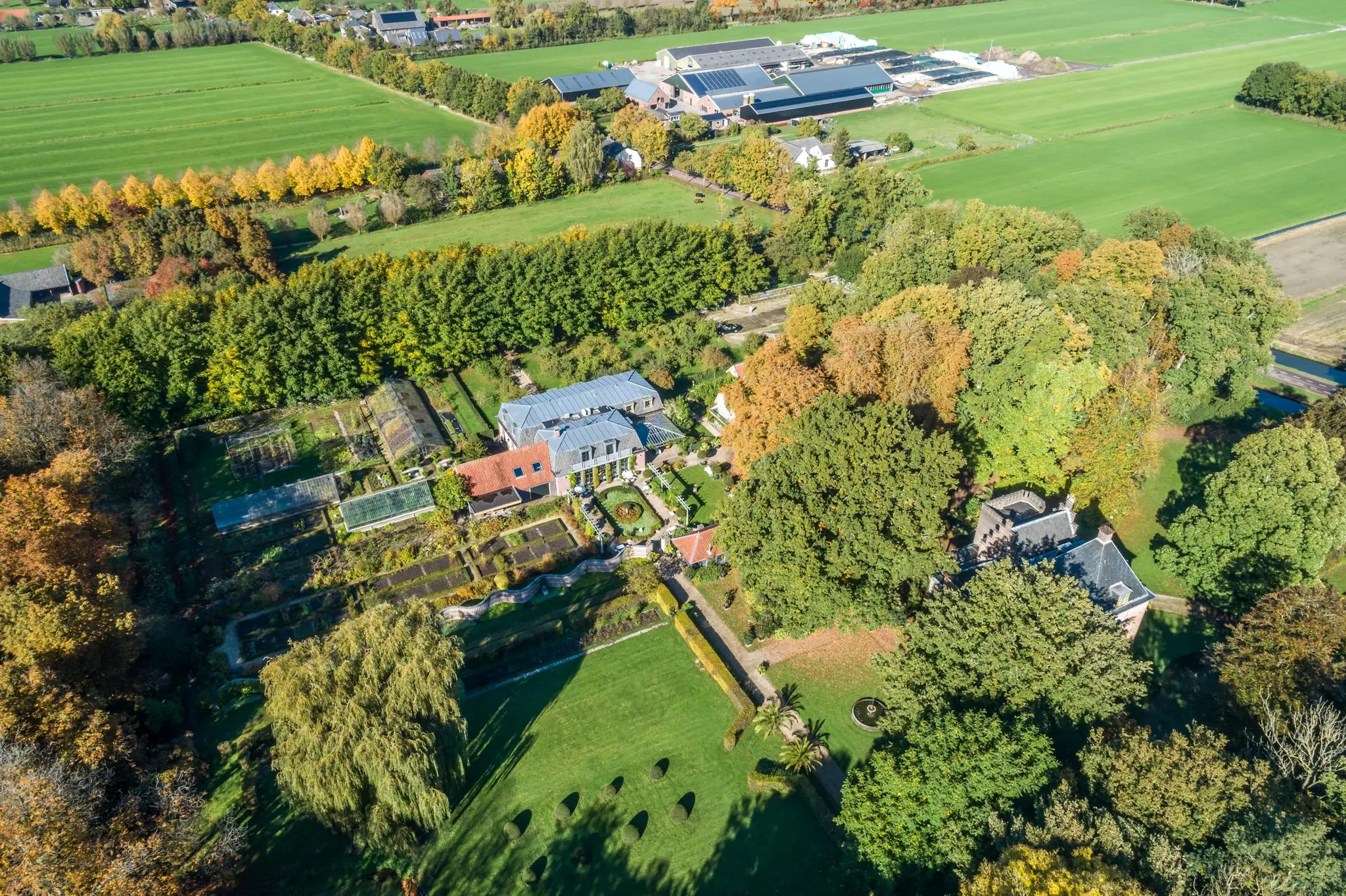 Luchtfoto van landgoed met monumentale boerderij en tuinen aan de Langbroekerdijk A, omringd door weilanden en bomen.